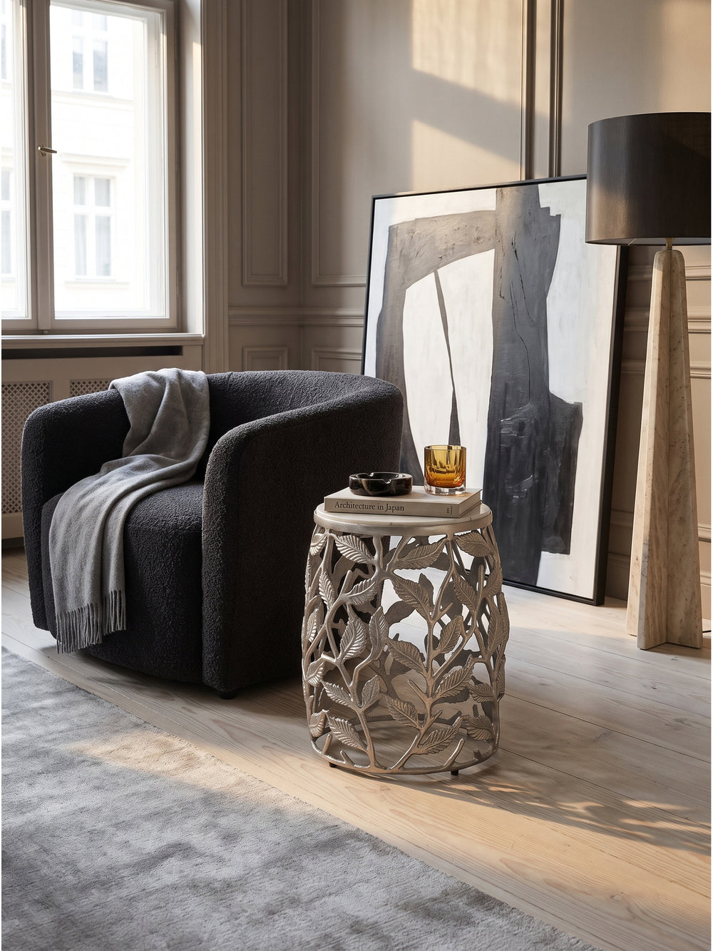 Der runde Beistelltisch aus silbernem Aluminium mit floralem Muster steht elegant im modernen Wohnzimmer neben einem grauen Sessel auf hellem Eichenparkett._