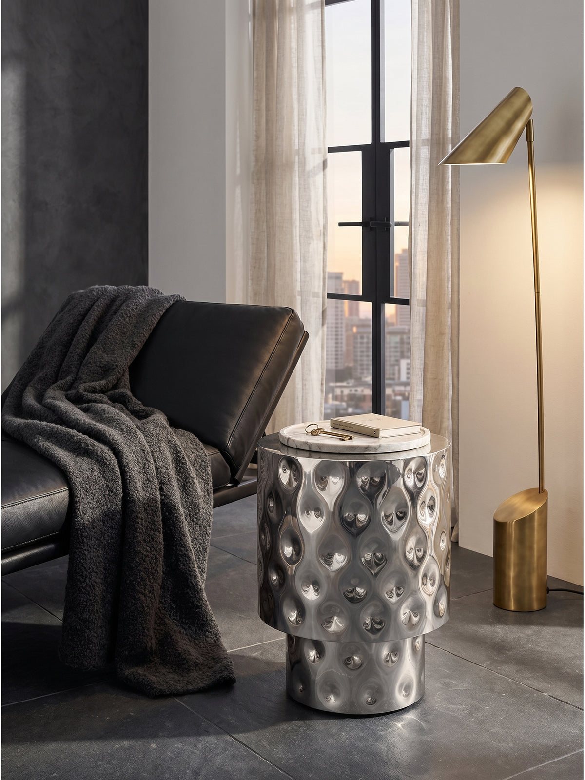 Der extravagante Beistelltisch aus Aluminium in Silber steht harmonisch neben einem modernen Design-Sessel vor bodentiefen Stahlrahmenfenstern.