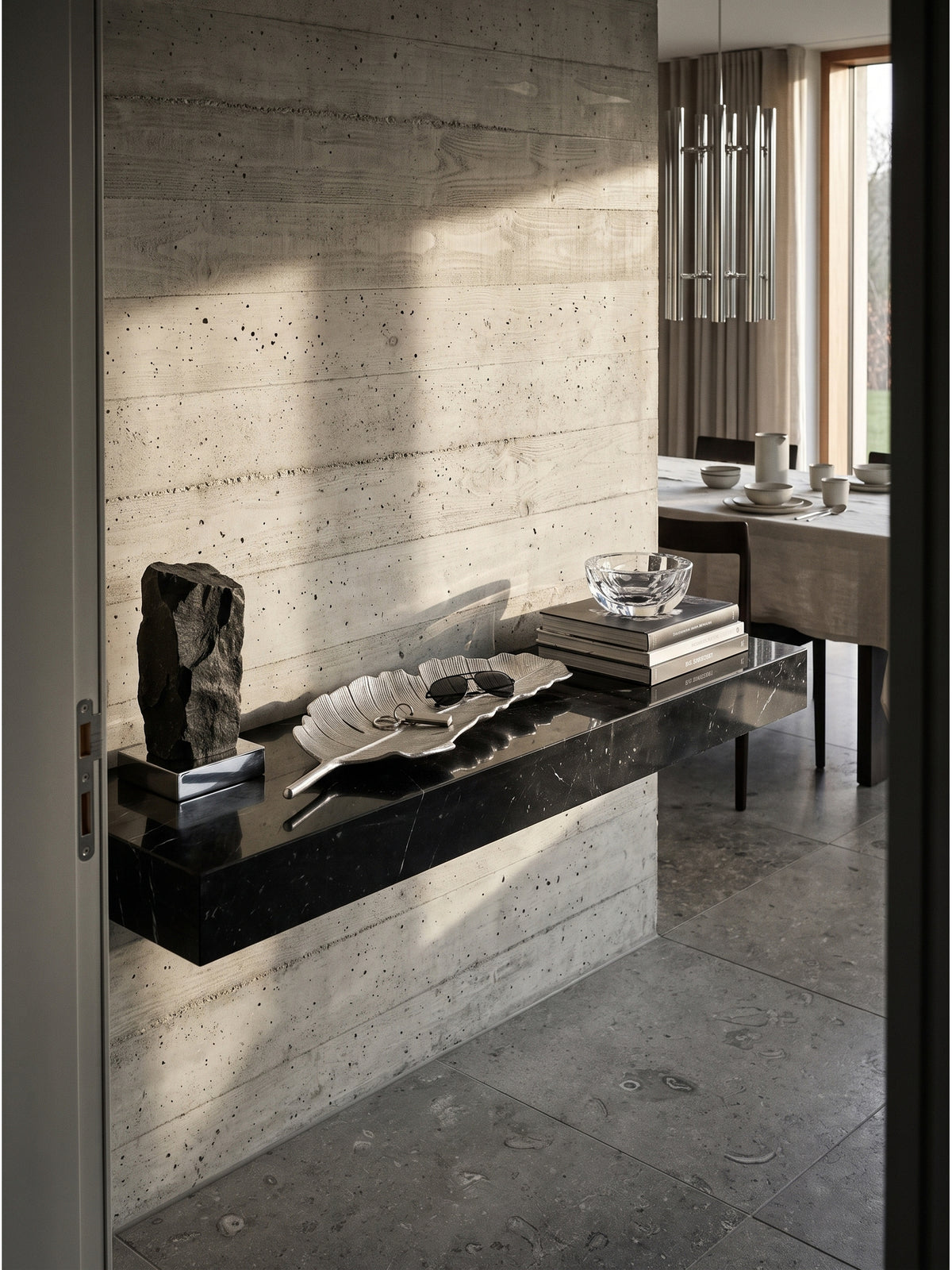 Große Dekoschale aus silbernem Aluminium 80cm in Blattform als architektonischer Blickfang auf einer schwebenden schwarzen Marmorkonsole im minimalistischen Flur._
