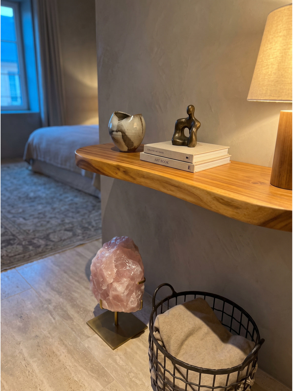 Dekoriertes Massivholzregal an einer beigen Wand mit einer handgefertigten Keramikvase und getrockneten Gräsern in einem minimalistisch eingerichteten Lesebereich_