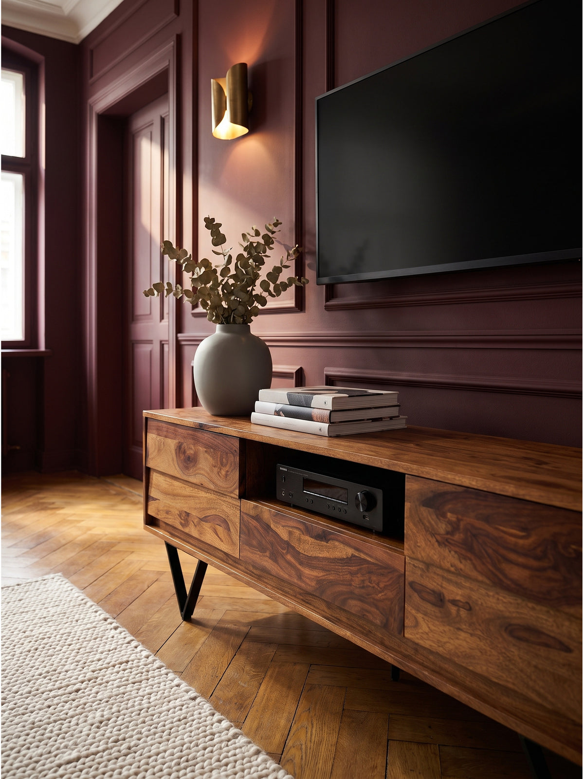 Gemütliches Detail auf dem Holz-Lowboard mit einer grauen Keramikvase und getrocknetem Eukalyptus im warmen Licht der Messing-Stehlampe_