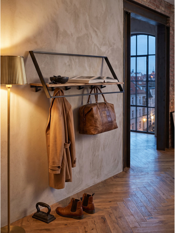 Ein sandfarbener Trenchcoat hängt an den robusten Metallhaken der Wandgarderobe, während auf der Holzablage ein Bildband liegt._