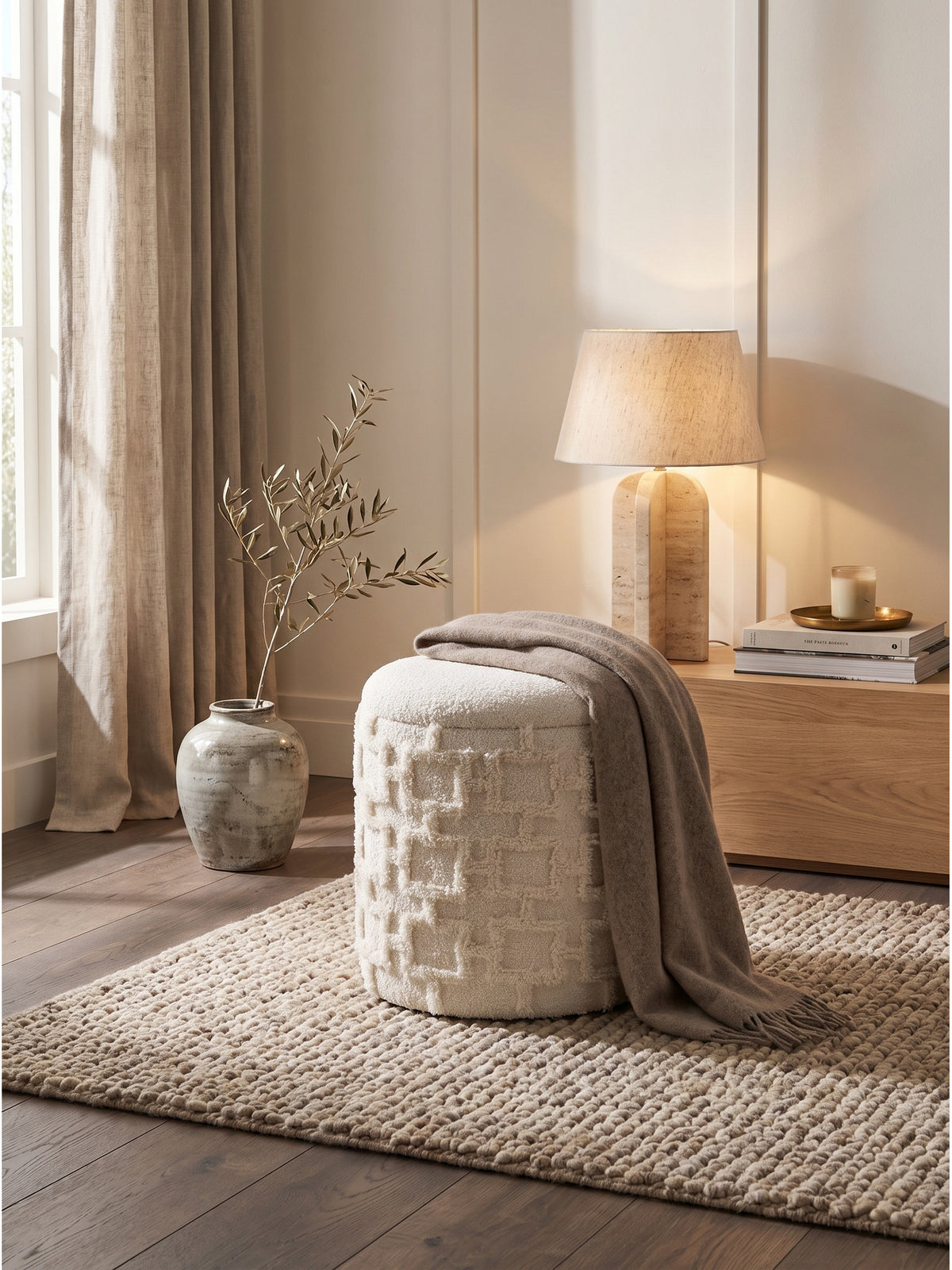 Flauschiger Stoffhocker in Creme kombiniert mit fließenden Leinenvorhängen und einem massiven Holzbett im Schlafzimmer.