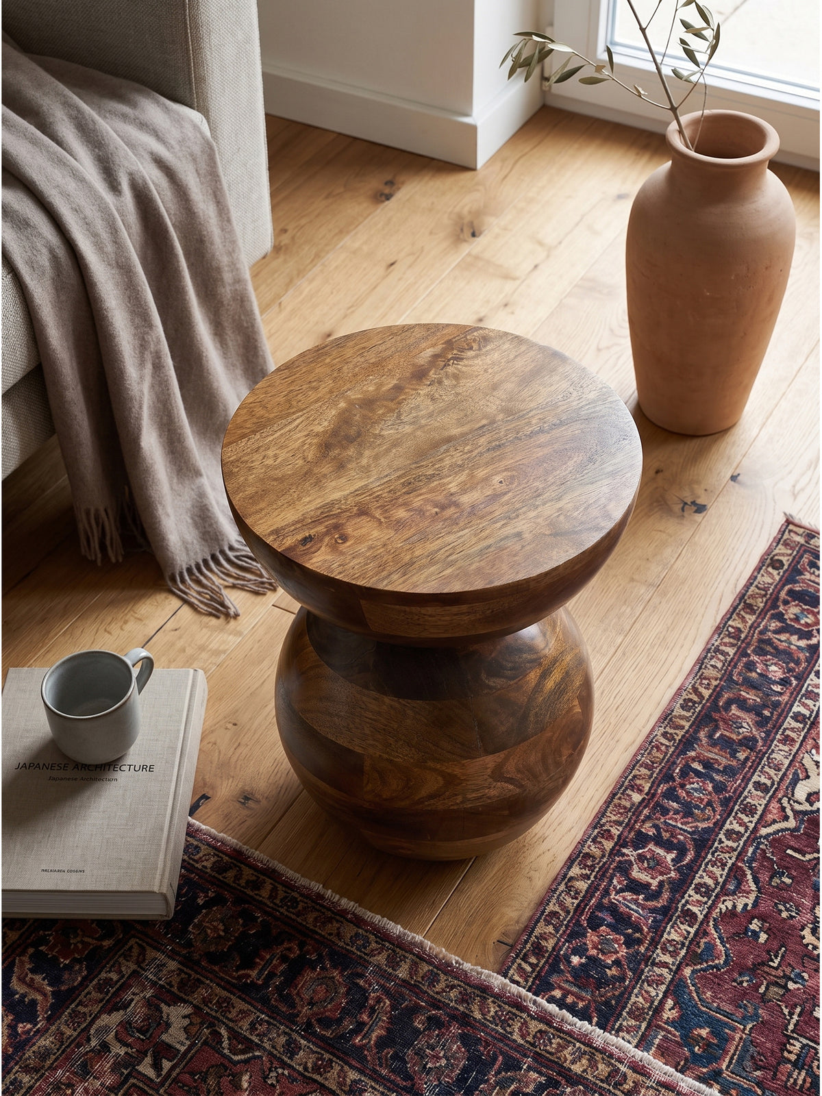 Runder Couchtisch aus Mangoholz mit auffälliger Maserung von oben fotografiert, arrangiert mit Architektur-Bildband und wabi-sabi Keramiktasse