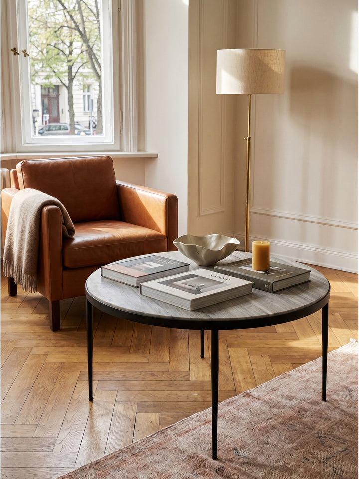 Puristischer Couchtisch mit Steinplatte kombiniert mit einem modernen anthrazitfarbenen Sofa und einer minimalistischen Stehlampe._