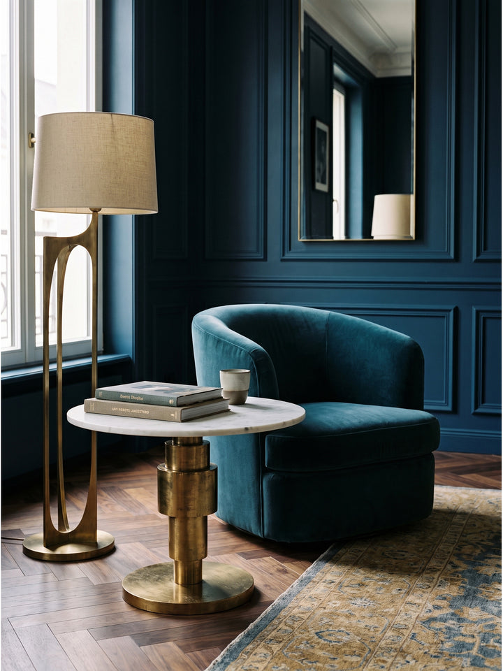 Der goldene Beistelltisch harmoniert perfekt mit einem tiefblauen Loungesessel und einer filigranen Messing-Stehlampe im stilvollen Ensemble_