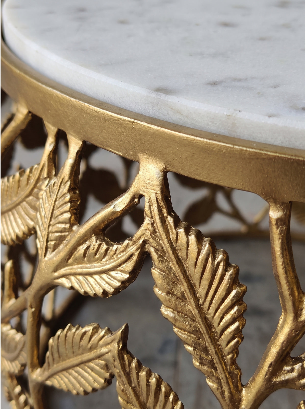 Nahaufnahme der natürlichen weißen Marmorierung der Tischplatte und des kunstvoll handgefertigten goldenen Aluminiumgestells in Blätterform_