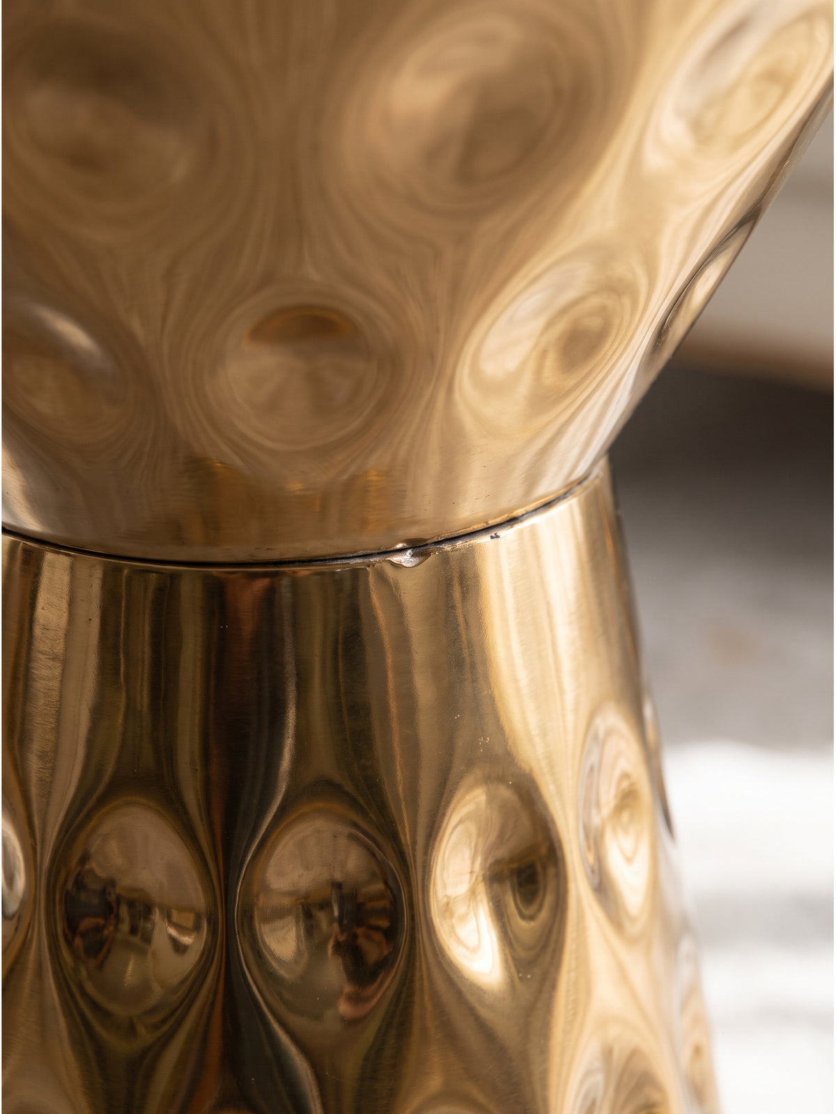 Nahaufnahme der gehämmerten Struktur des Beistelltischs aus Aluminium in Gold mit Lichtreflexionen auf der strukturierten Oberfläche_