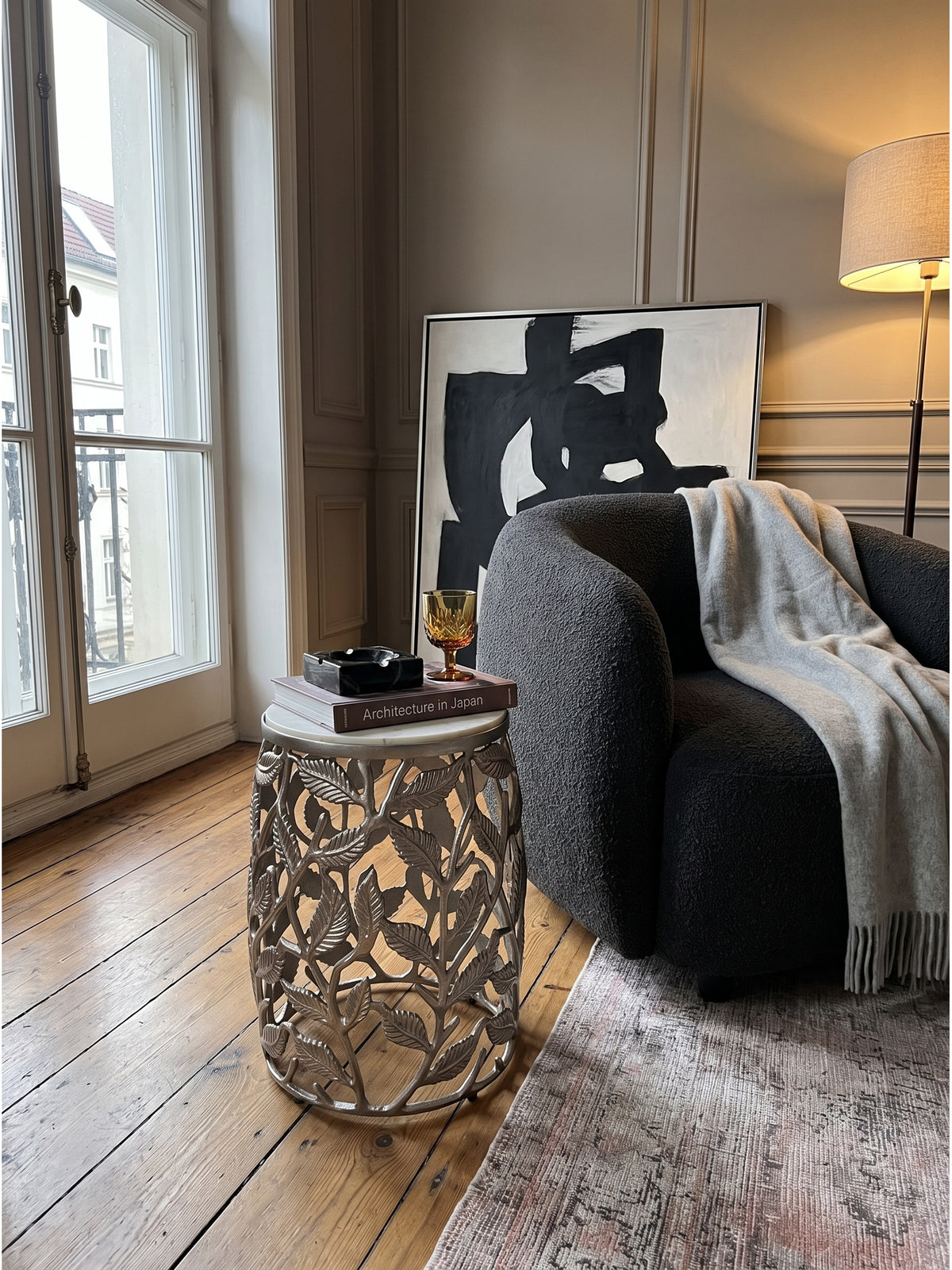 Ein dunkler Bouclé-Sessel ergänzt den runden Design-Tisch mit silbernem Metallgestell in einer luxuriösen Raumecke mit dezenten Wandleisten.