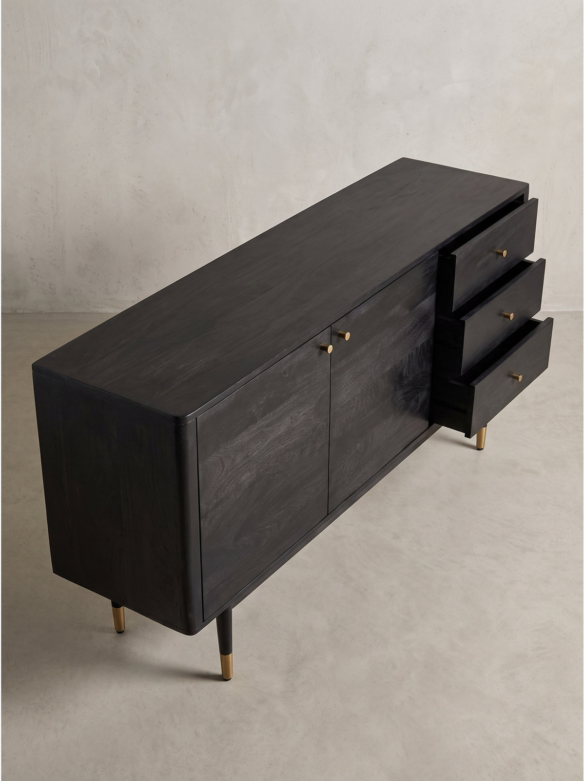 Leicht schräge Perspektive der modernen Massivholz-Kommode in Schwarz mit markanten konischen Beinen und goldenen Füßen.