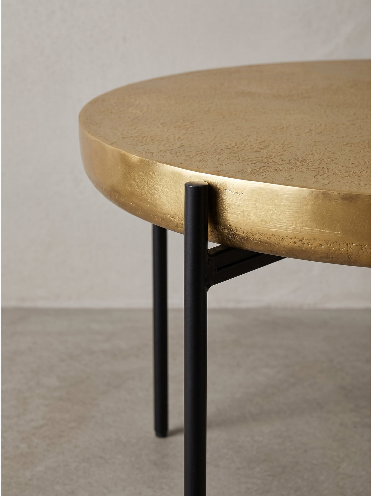 Schrägansicht des eleganten runden Tisches für das Wohnzimmer mit edler Goldstruktur und stabilen schwarzen Beinen_