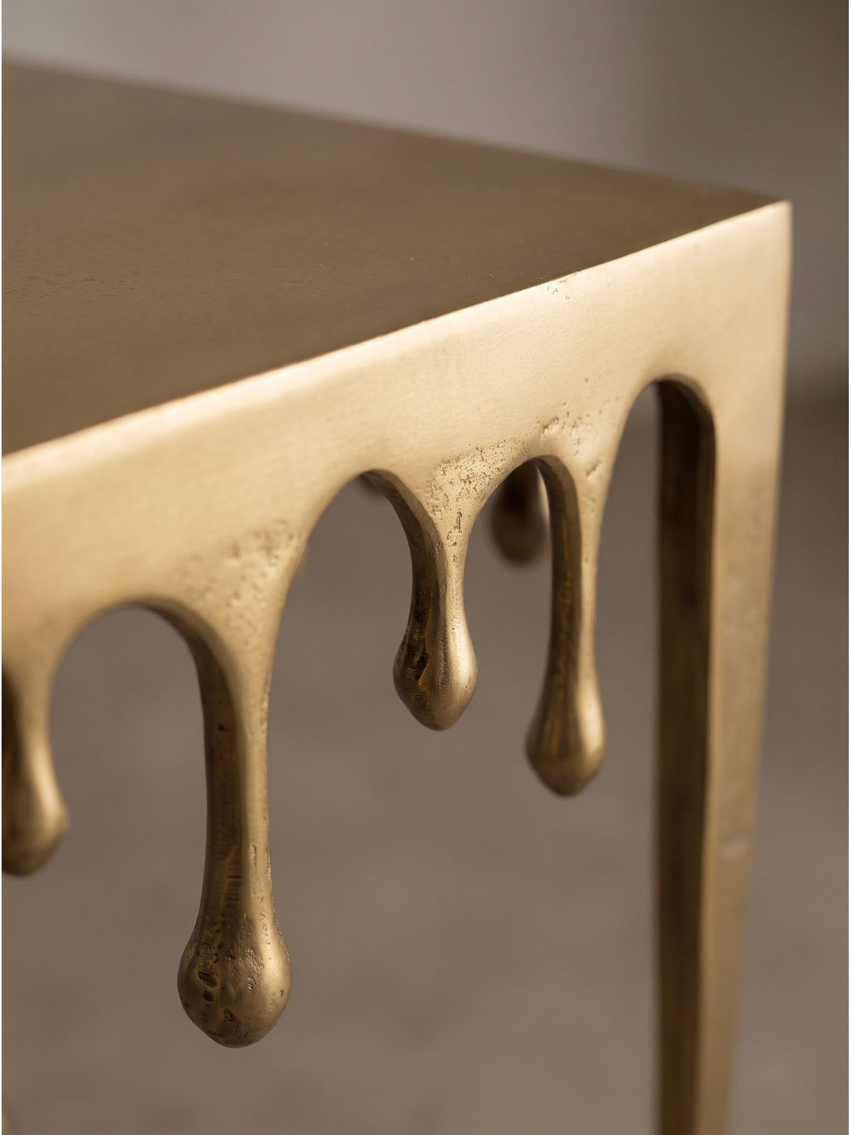 Nahaufnahme der glatten goldenen Aluminiumoberfläche des Beistelltischs mit kunstvollen schmelzenden Kanten_