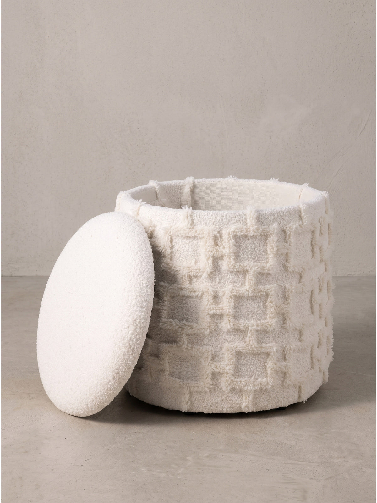 Leicht erhöhte Ansicht auf den gemütlichen Fußhocker in Creme, die den gepolsterten Deckel und die runde Form betont._