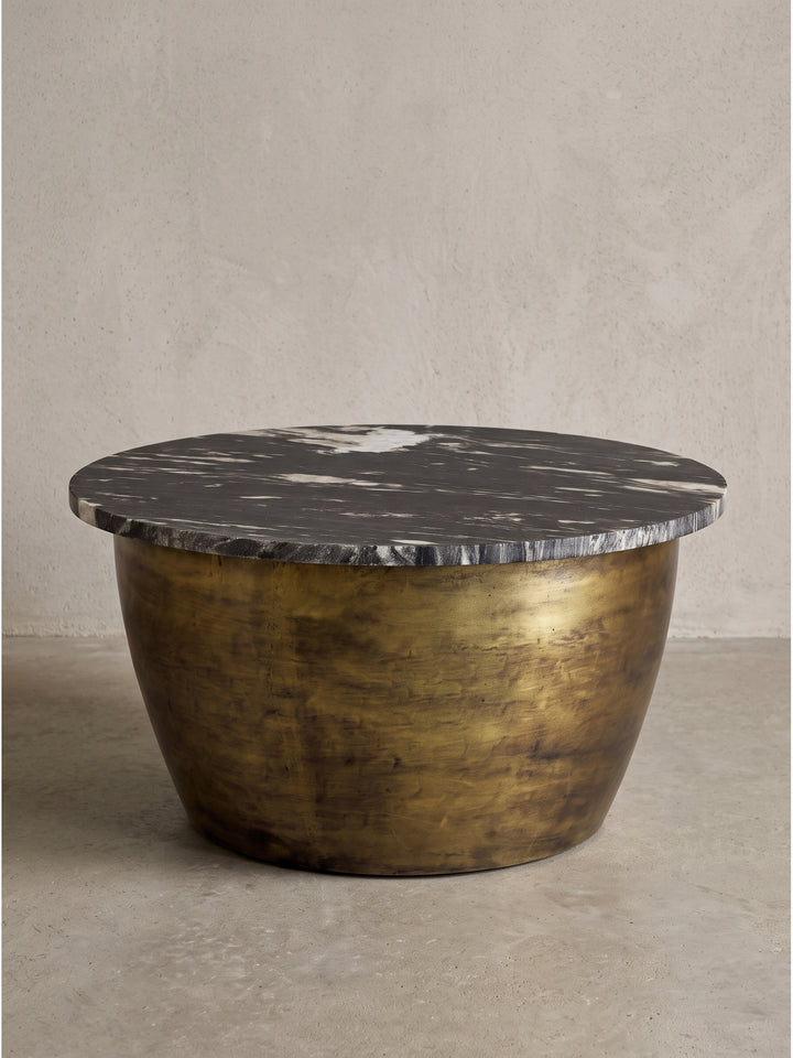 Fokussierte Detailansicht auf die Kante der massiven dunklen Marmorplatte, die auf dem warm schimmernden runden Eisengestell des Tisches aufliegt_