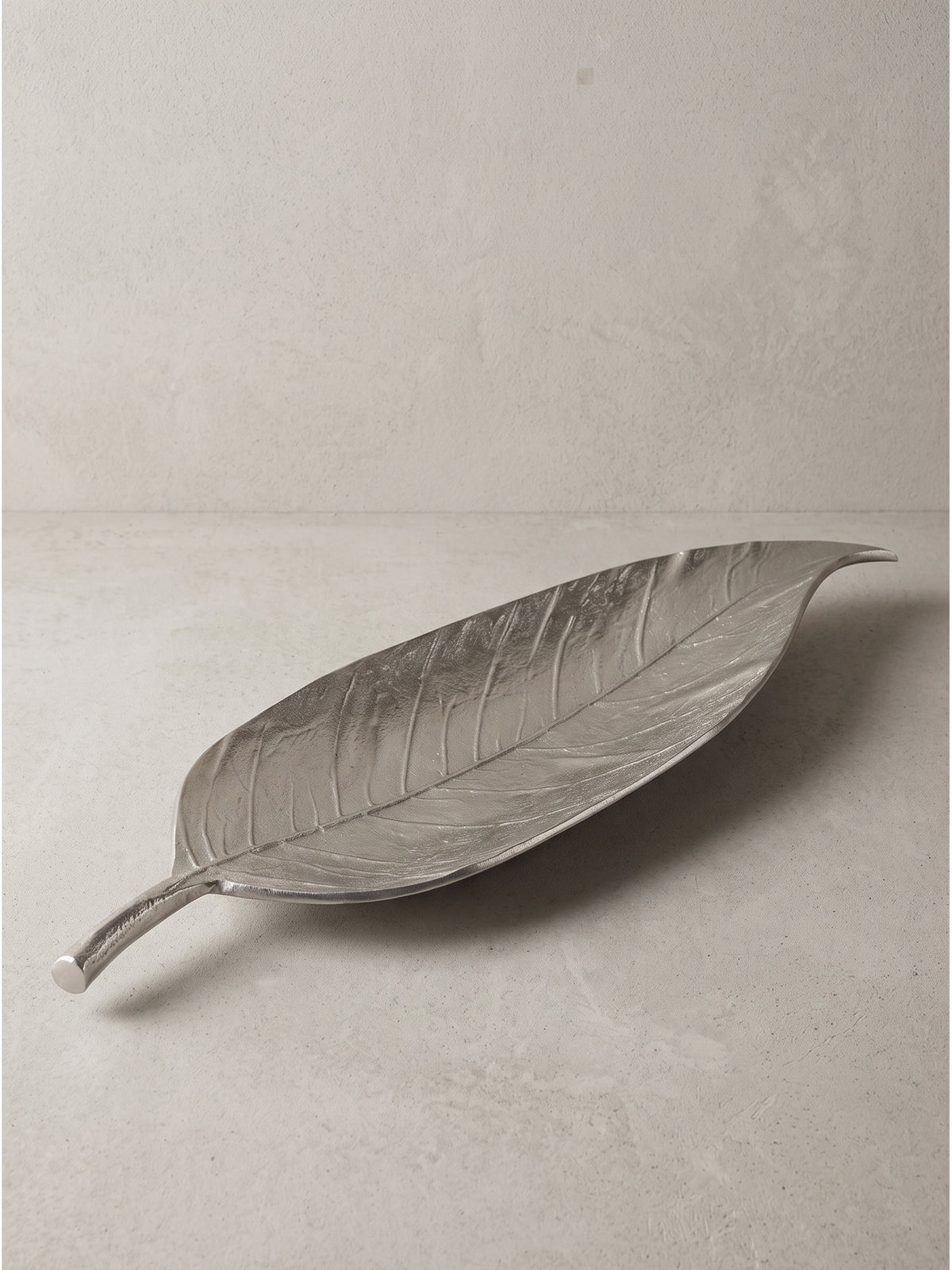 Detailansicht des geschwungenen Stiels der Dekoschale Blatt aus silbernem Aluminium auf neutralem Hintergrund