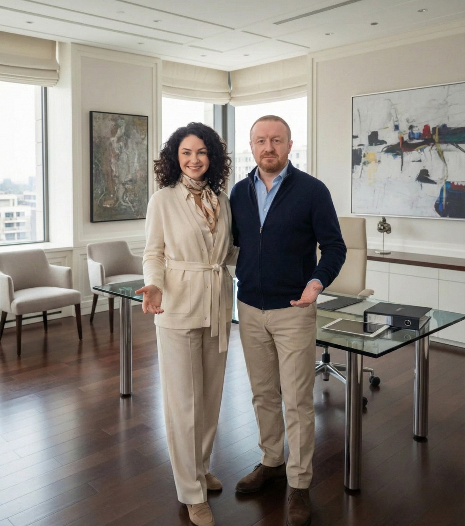 Porträt der Gründer von Kadima Design in einem eleganten Büro - eine Frau in beigem Anzug und ein Mann im grauen Anzug stehen vor einem modernen Schreibtisch mit Glasplatte, umgeben von zeitgenössischer Kunst und Designermöbeln