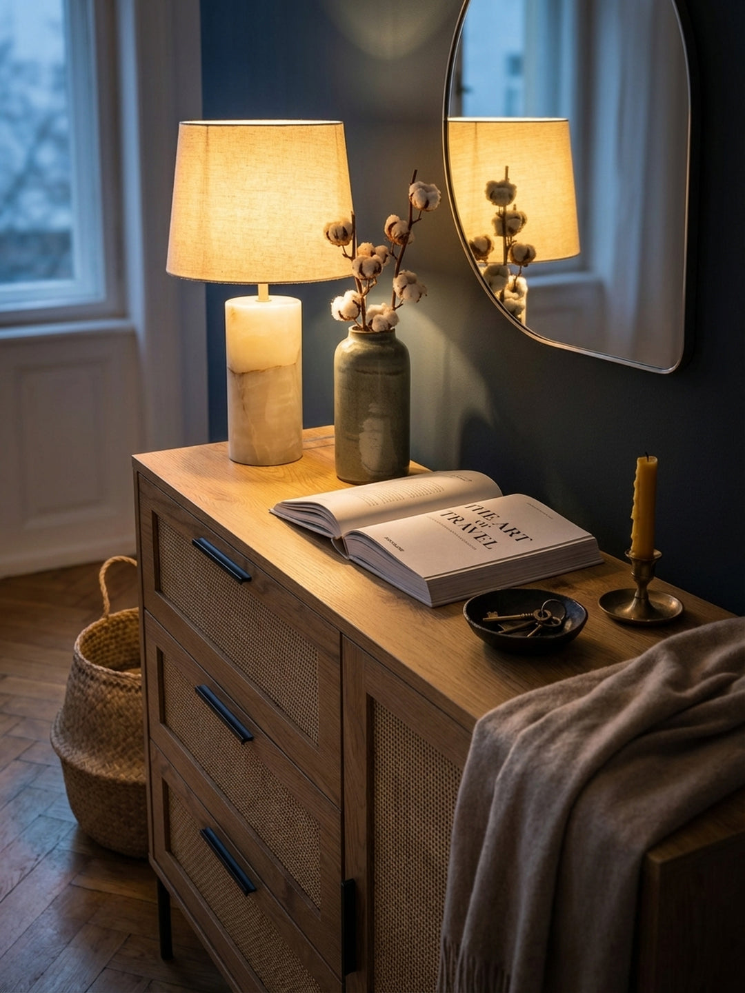 Vignette einer Anrichte mit Rattan-Fronten, dekoriert mit einer handgetöpferten Keramikvase und einem Stapel Leinen-Notizbücher, für eine wohnliche Atmosphäre im Eingangsbereich._