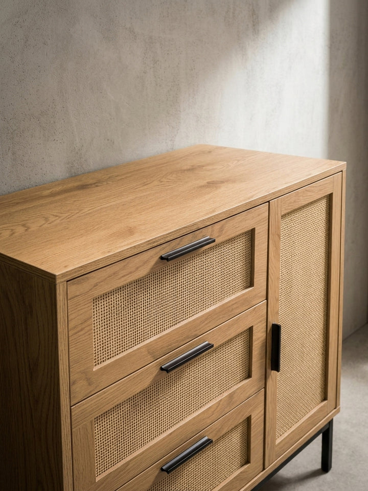 Alternative Perspektive der Kommode im Boho-Stil, die den Kontrast zwischen dem warmen Holzton, dem hellen Rattan und den mattschwarzen Griffen betont._