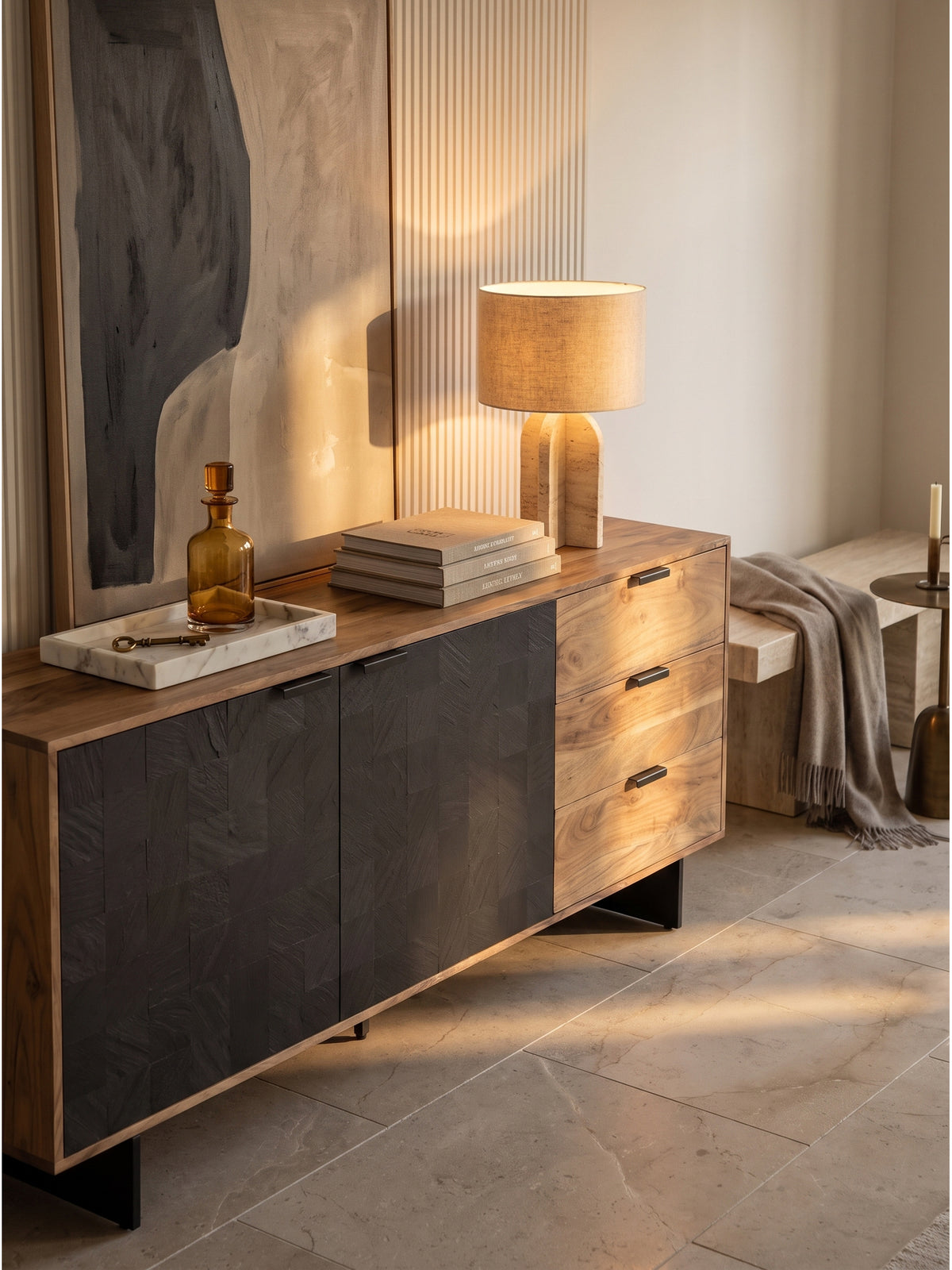 Elegante Dekoration auf der 175 cm breiten Massivholz-Kommode mit einer Travertinlampe und Kunstbänden in einem lichtdurchfluteten Raum._