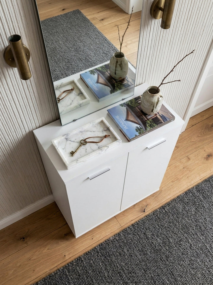 Erhöhte Perspektive auf den mattweißen Flurschrank im Eingangsbereich, elegant kombiniert mit einem Calacatta-Marmor-Tablett und messingfarbener Wandleuchte_