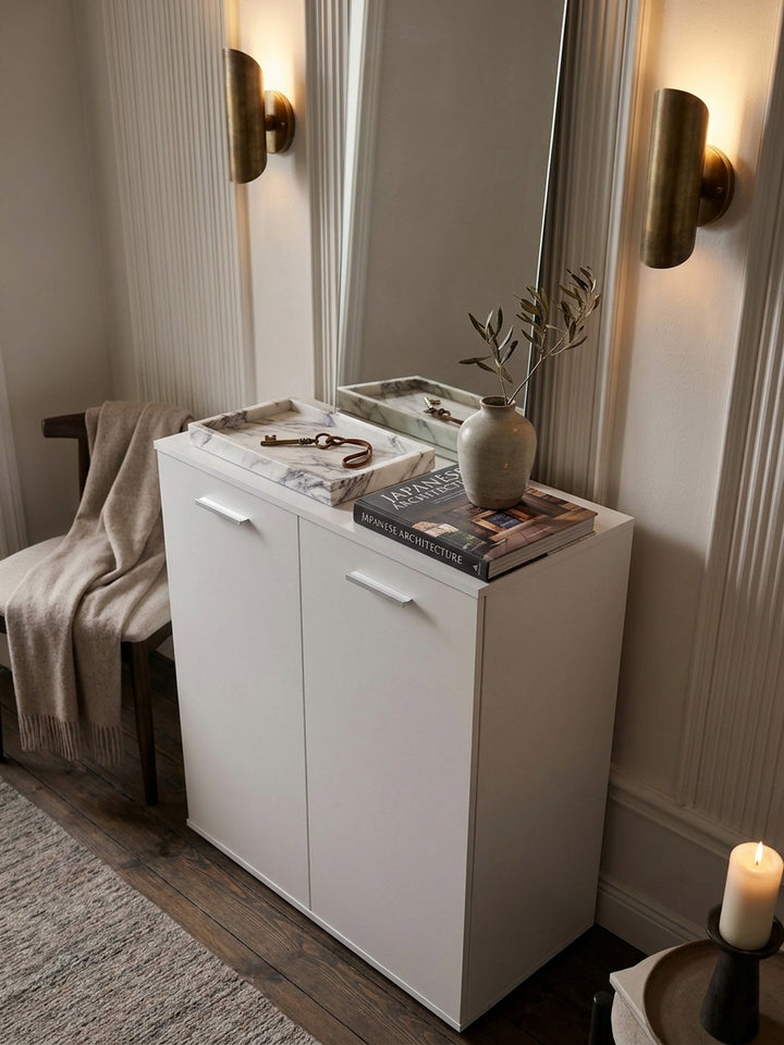 Stilvoll dekoriertes Sideboard in Weiß mit einem schweren Bildband über Architektur, einer handgefertigten Keramikvase und warmem Licht einer Tischlampe_