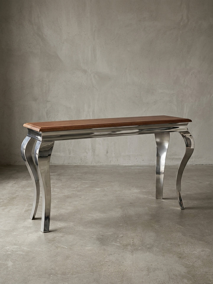 Moderner Konsolentisch freigestellt in der Frontalansicht. Die 130x76 cm große Anrichte kombiniert eine massive Echtholzplatte mit vier glänzenden, barock geschwungenen Metallbeinen._