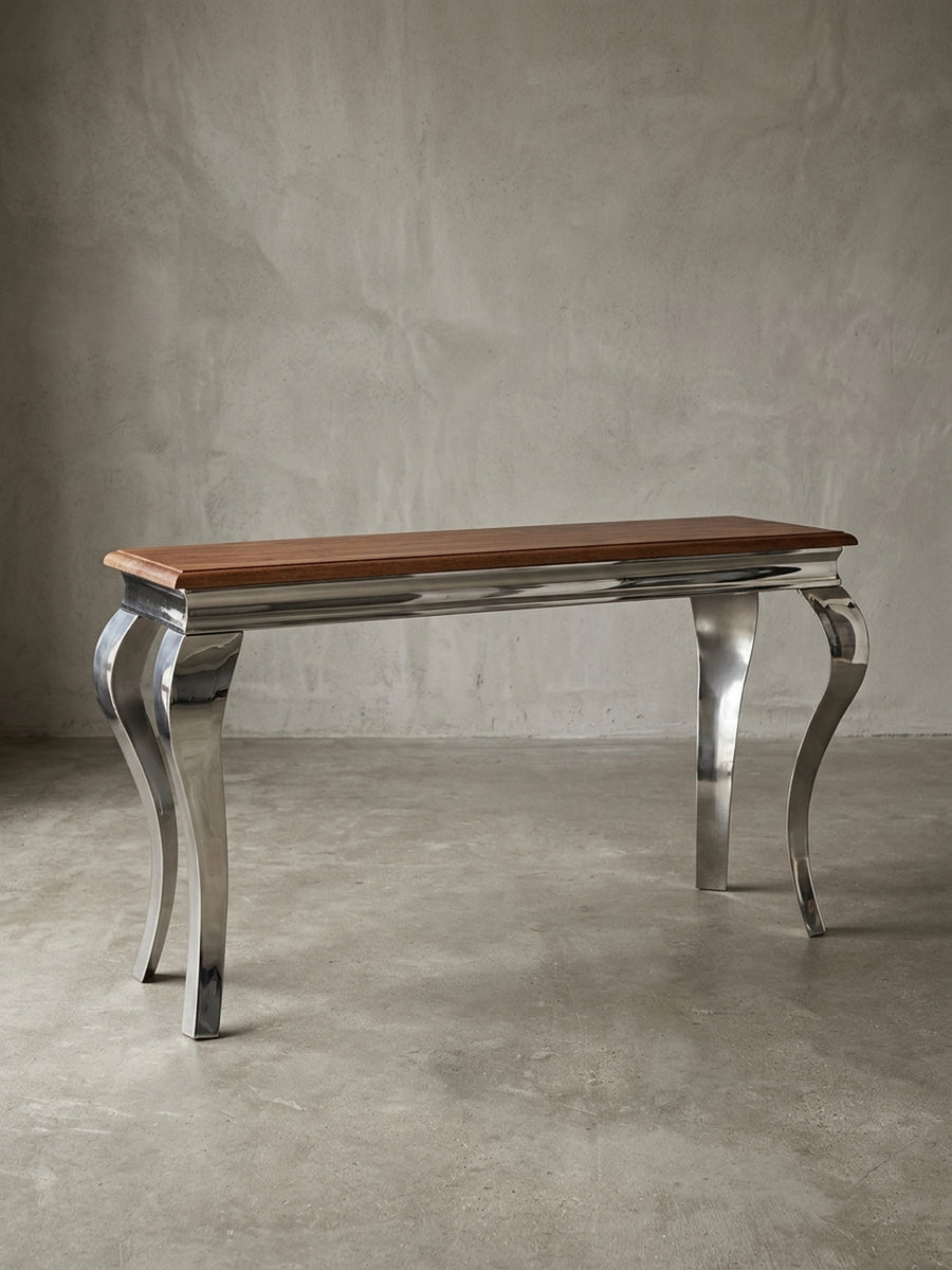 Moderner Konsolentisch freigestellt in der Frontalansicht. Die 130x76 cm große Anrichte kombiniert eine massive Echtholzplatte mit vier glänzenden, barock geschwungenen Metallbeinen._
