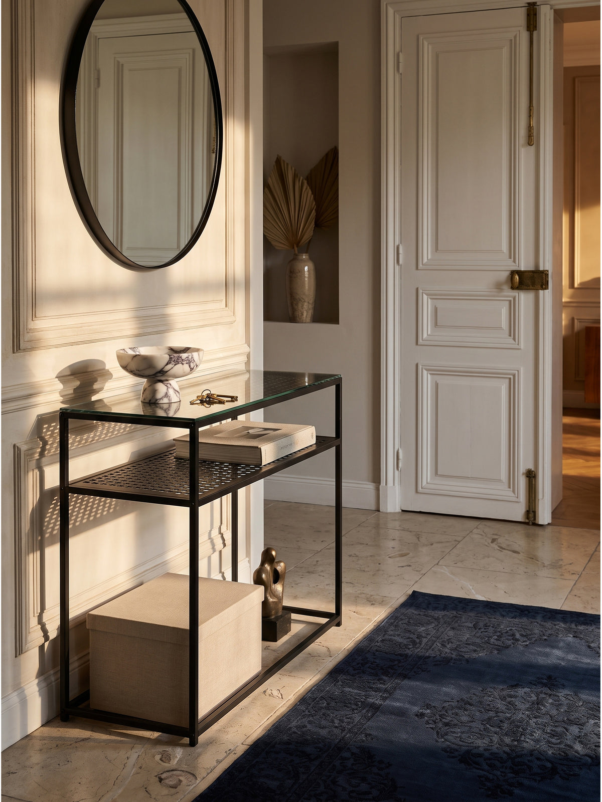 Schwarzer Konsolentisch aus Metall und Glas im eleganten Eingangsbereich mit großem runden Spiegel an einer warmweißen Wand
