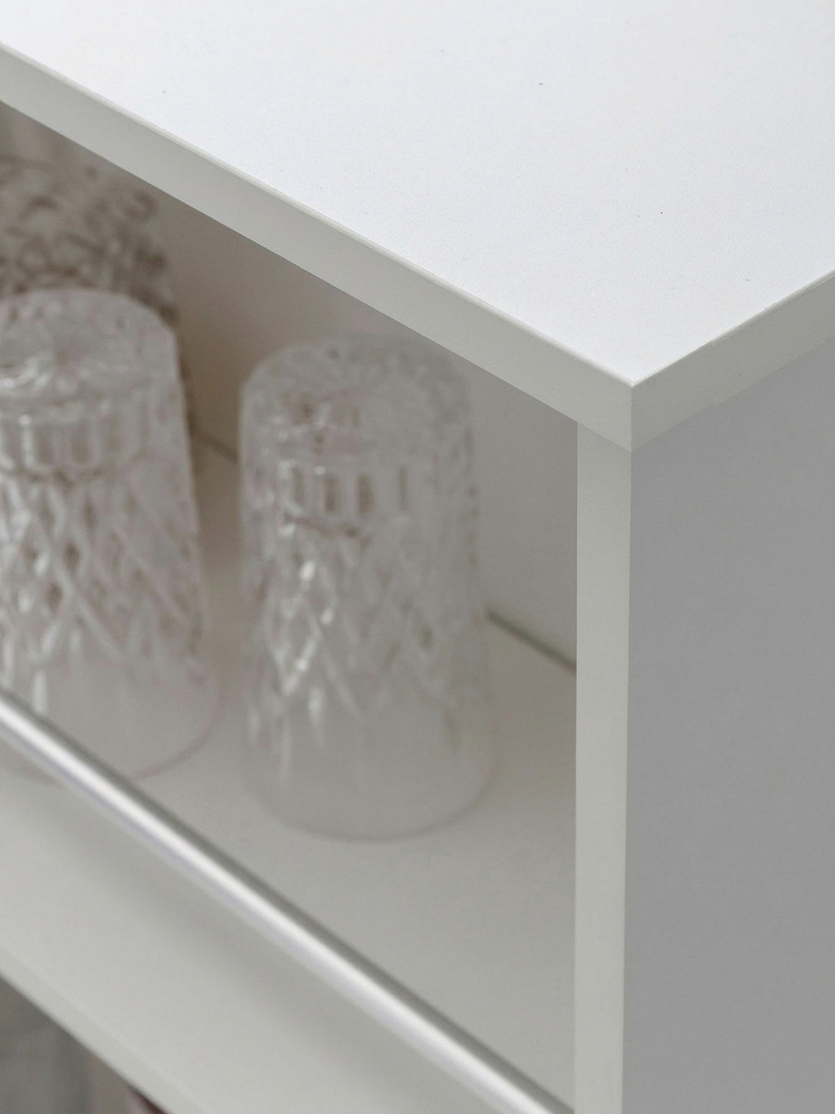 Nahaufnahme der Regalabschlüsse am weißen Tresentisch. Die filigranen Haltestreben aus Aluminium in den 33cm hohen Fächern verhindern das Herausfallen von Flaschen oder Gläsern._