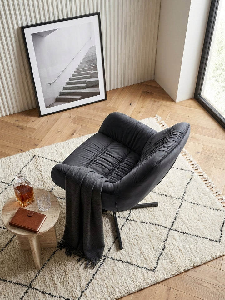 Blick von oben auf eine elegante Leseecke mit schwarzem Samtsessel auf einem cremefarbenen Vintage-Teppich neben einem runden Messing-Beistelltisch._