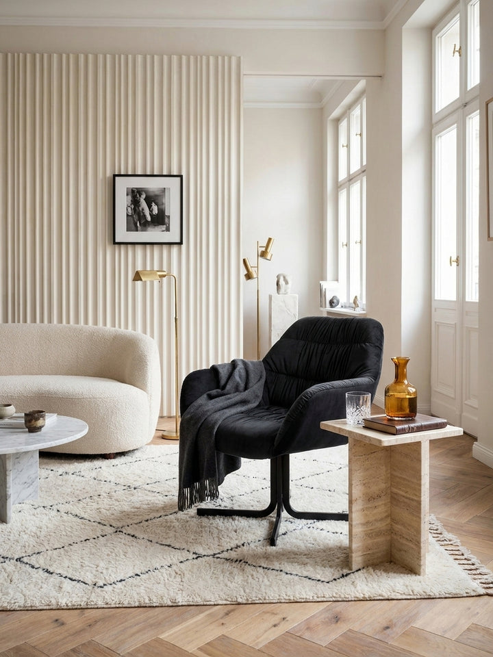 Schwarzer Design-Clubsessel mit Samtbezug stilvoll kombiniert mit einem puristischen Leinensessel und einer eleganten Alabaster-Stehleuchte vor einer geriffelten Wand._