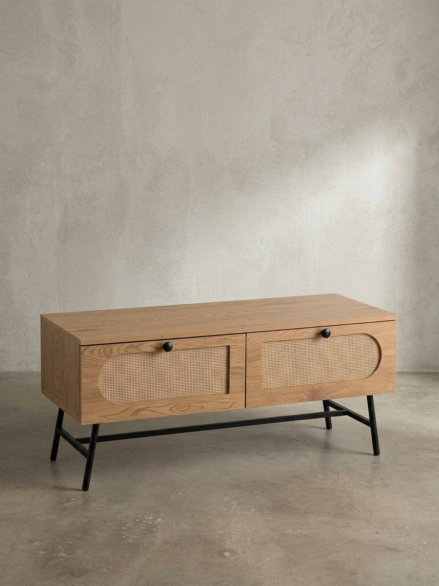 Frontansicht des TV-Schranks mit Eiche-Dekor, zwei Rattan-Schubladen und schwarzen Metallbeinen, freigestellt vor weißem Hintergrund._