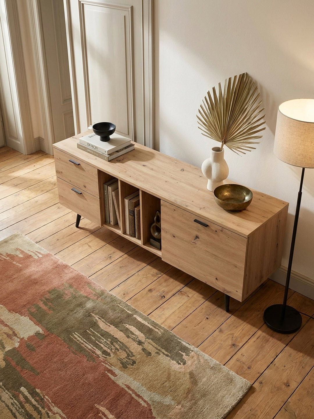 Draufsicht auf eine elegante TV-Kommode in heller Holzoptik mit schwarzen Metallfüßen und geräumigen Fächern neben einem Wollteppich._