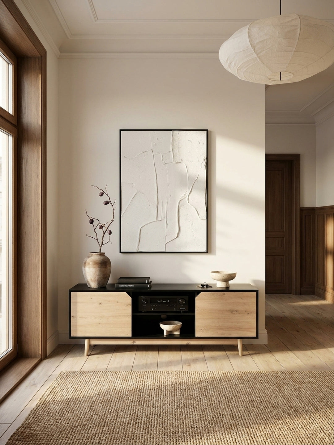 Weitläufige Ansicht eines minimalistischen Wohnzimmers im Japandi-Stil mit einem Lowboard in Schwarz und Eiche-Dekor unter einem gerahmten Kunstwerk._