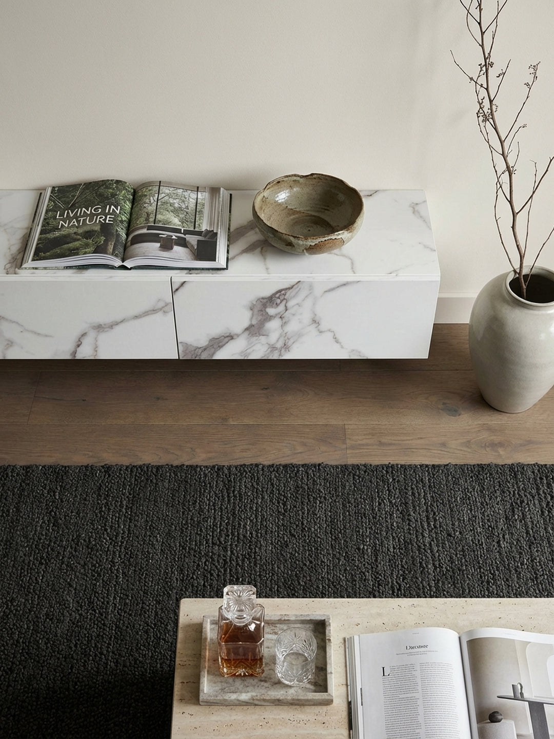 Draufsicht auf ein modernes Wohnzimmer-Arrangement mit dem schwebenden Fernsehschrank in Marmor-Optik als zentrales Element auf einem dunklen Teppich._
