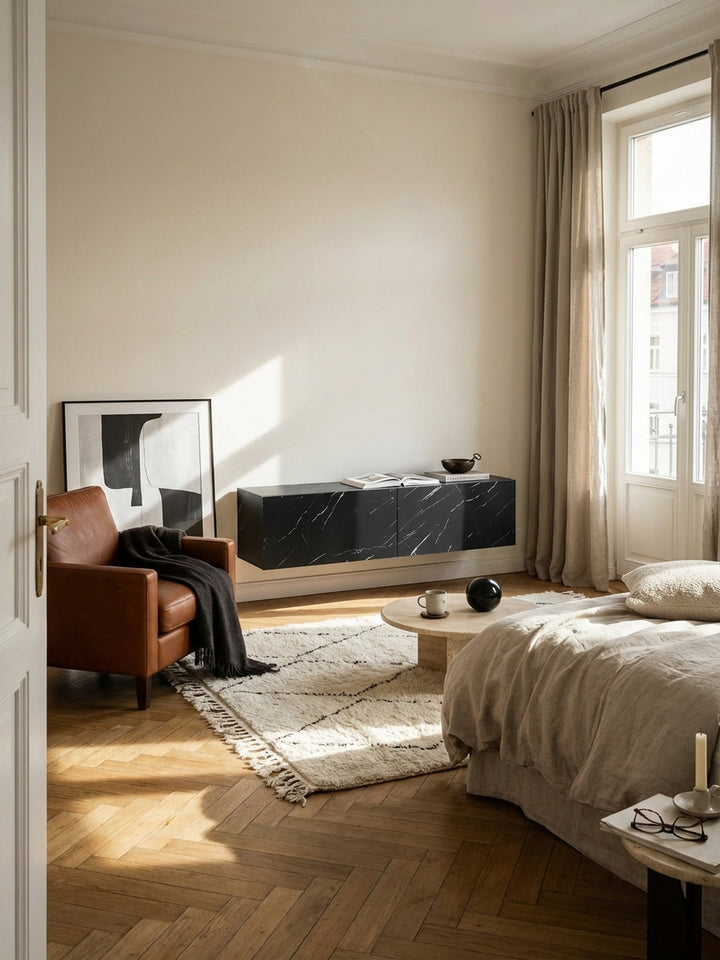 Das hängende Lowboard in schwarzer Marmor-Optik als eleganter Mittelpunkt in einem minimalistischen Wohnzimmer mit Eichenparkett und hoher Decke._