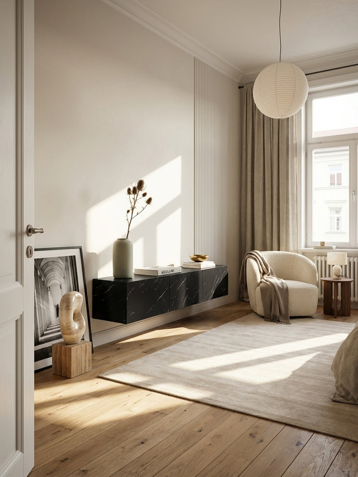 Modernes Wohnzimmer mit einem schwebenden TV-Lowboard in schwarzer Marmor-Optik, montiert an einer hellen Wand über einem beigen Teppich und Holzboden._