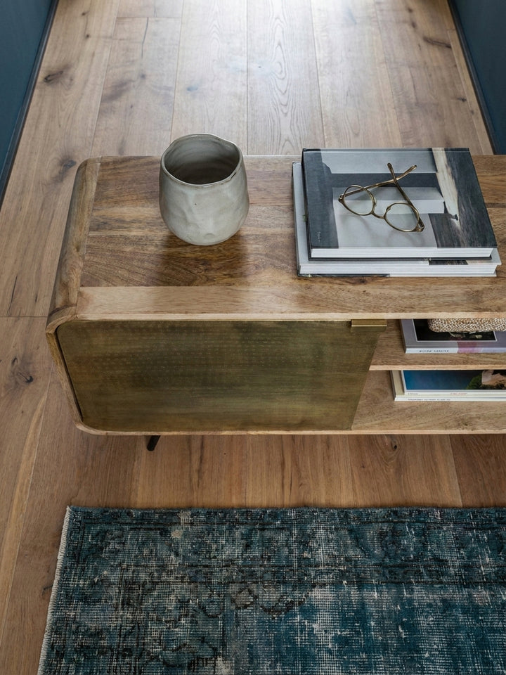 Draufsicht auf ein Wohnzimmer mit einem 160 cm breiten TV-Schrank aus Mango Massivholz als Mittelpunkt auf einem alten türkischen Teppich vor einem grauen Sofa._