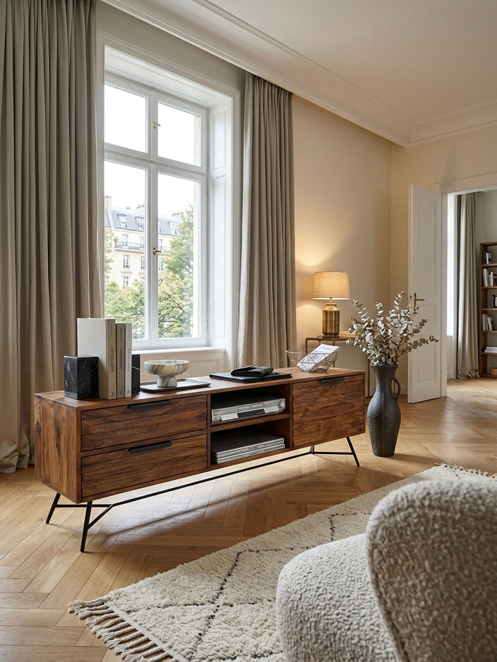 Massives TV-Lowboard aus edlem Sheesham-Holz im luxuriösen Wohnzimmer. Das 160cm breite Hifi-Board mit schwarzen Metallbeinen steht auf einem hellen Wollteppich vor einer cremeweißen Wand._