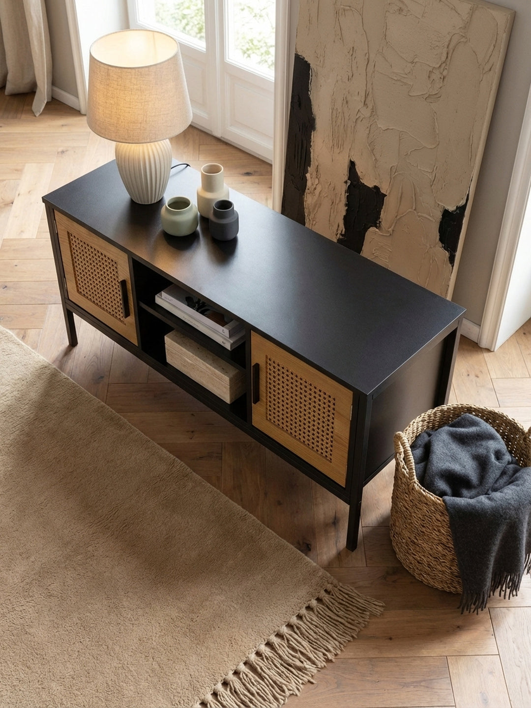 Von oben fotografierte Wohnzimmereinrichtung mit TV-Schrank aus schwarzem Holz und Rattan, platziert auf einem Dielenboden aus heller Eiche._