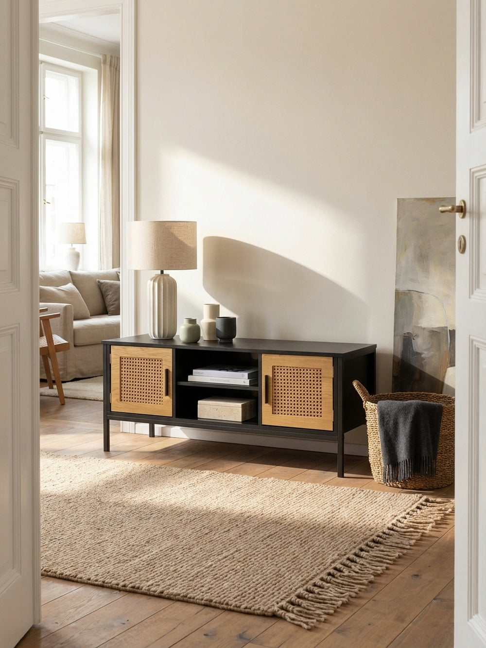 Schwarzes TV-Lowboard mit Eiche-Türen und Wiener Geflecht in einem hellen Wohnzimmer mit Sandfarbenem Wollteppich und bequemen Sofa._