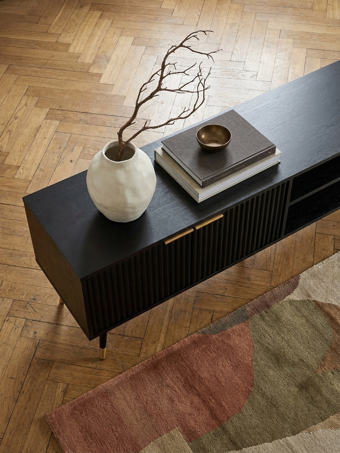 Draufsicht auf ein Design-Lowboard mit 150 cm Breite, arrangiert mit Dekoration auf einem Teppich in einem modern eingerichteten Wohnbereich._