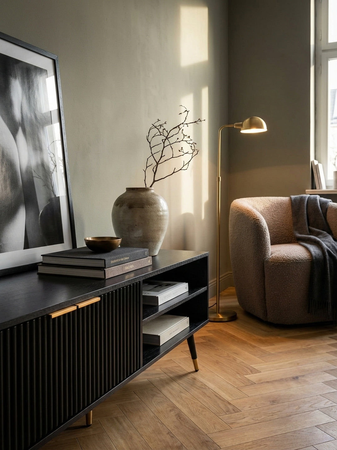 Detailansicht des schwarzen TV-Schranks mit einem Receiver im offenen Fach und einer Vase mit Baumwollzweigen auf der Ablagefläche._
