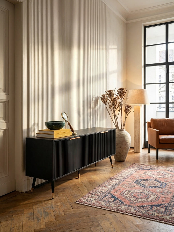 Modernes schwarzes TV-Lowboard mit Rillenfront und Messinggriffen, zentral platziert in einem lichtdurchfluteten Altbau-Wohnzimmer auf Fischgrätparkett._