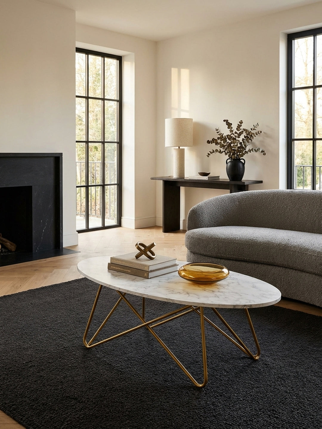 Eleganter ovaler Couchtisch in weißer Marmoroptik mit goldenem Metallgestell, stilvoll inszeniert vor einem grauen Sofa auf einem beigen Teppich in einem hellen Wohnzimmer._