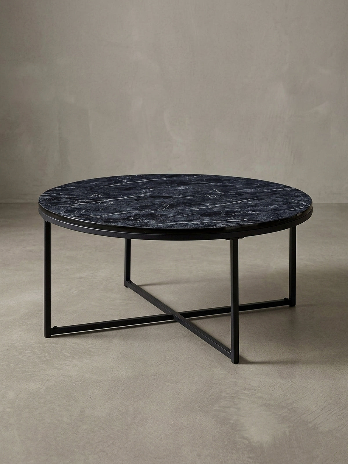 Design-Couchtisch in 3/4-Ansicht, die runde schwarze Marmor-Optik Platte und das gekreuzte Stahlgestell betonend, ideal für das moderne Wohnzimmer.
