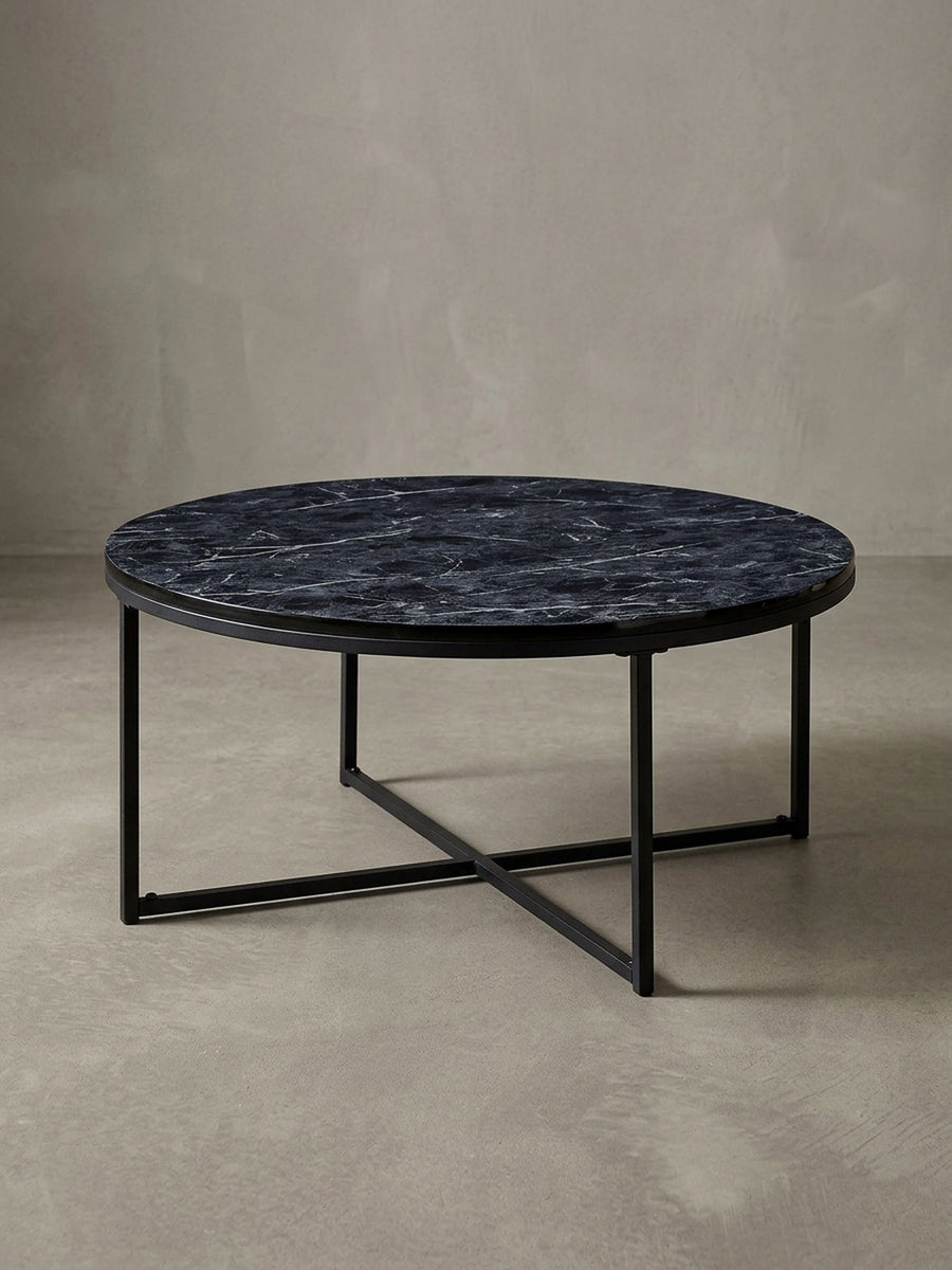 Design-Couchtisch in 3/4-Ansicht, die runde schwarze Marmor-Optik Platte und das gekreuzte Stahlgestell betonend, ideal für das moderne Wohnzimmer._