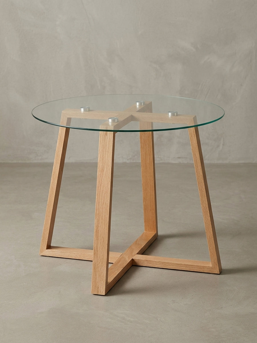Design-Sofatisch Eiche massiv in 3/4-Ansicht. Das über Kreuz gestaltete Holzgestell und die runde Glasplatte des 47 cm hohen Kaffeetisches sind gut zu erkennen._