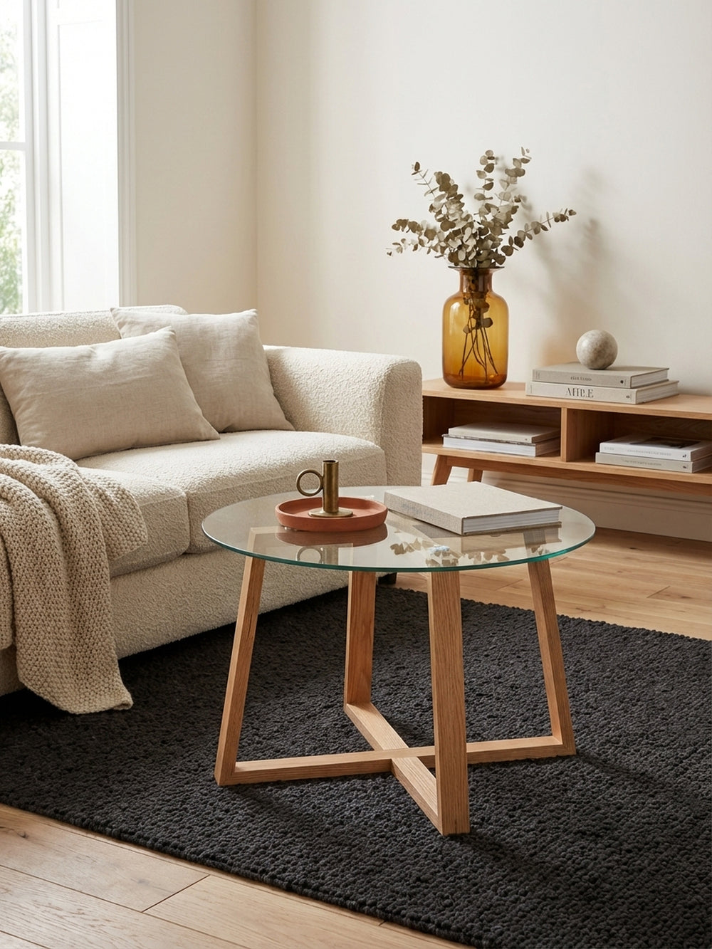 Couchtisch aus Eiche mit Glasplatte in einem modernen Wohnzimmer neben einem Sofa. Der runde Sofatisch (58x47cm) steht auf einem dunklen Teppich und schafft eine warme Atmosphäre._