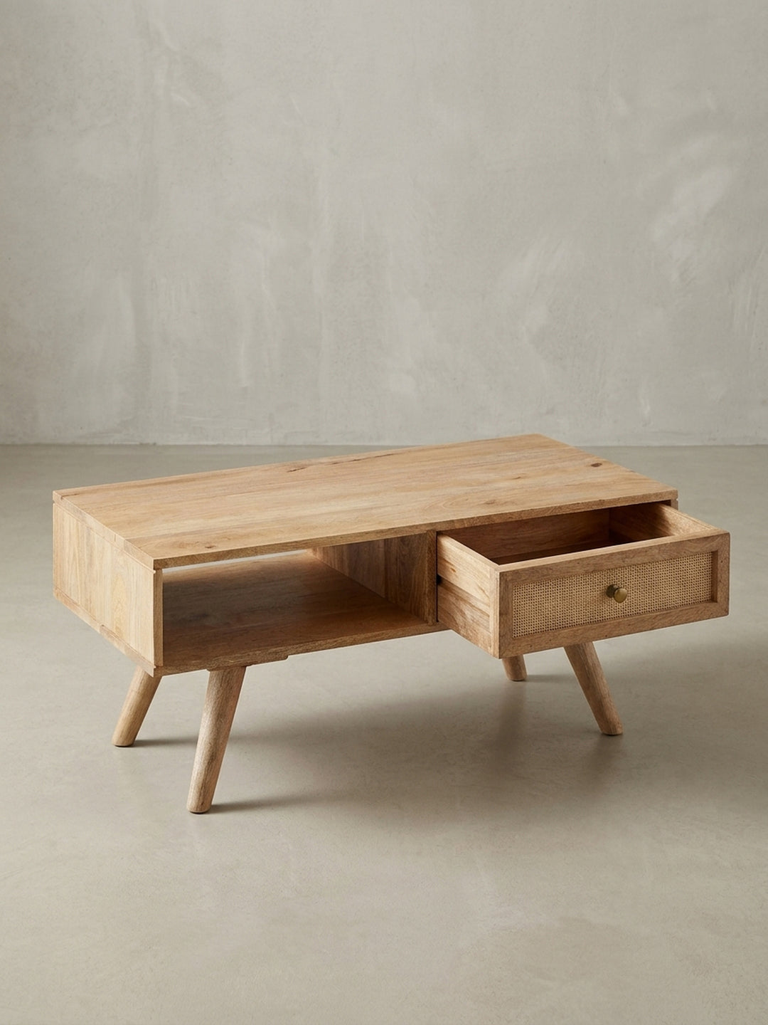 Massiver Sofatisch aus Mangoholz schräg von oben fotografiert, um die glatte Tischplatte und den Kontrast zum geflochtenen Rattan der Schublade zu zeigen._